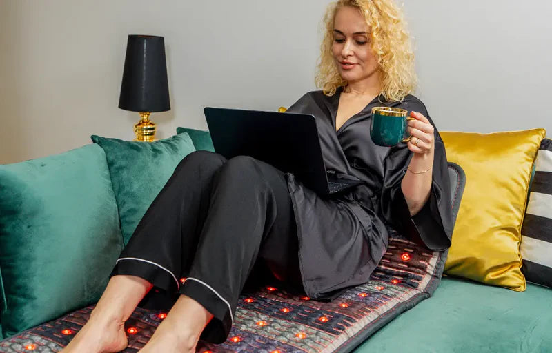 Blondynka w czarnej piżamie siedzi na materacu Dr. Stone PRO. Pracuje na laptopie. W lewej dłoni trzyma zielony kubek.